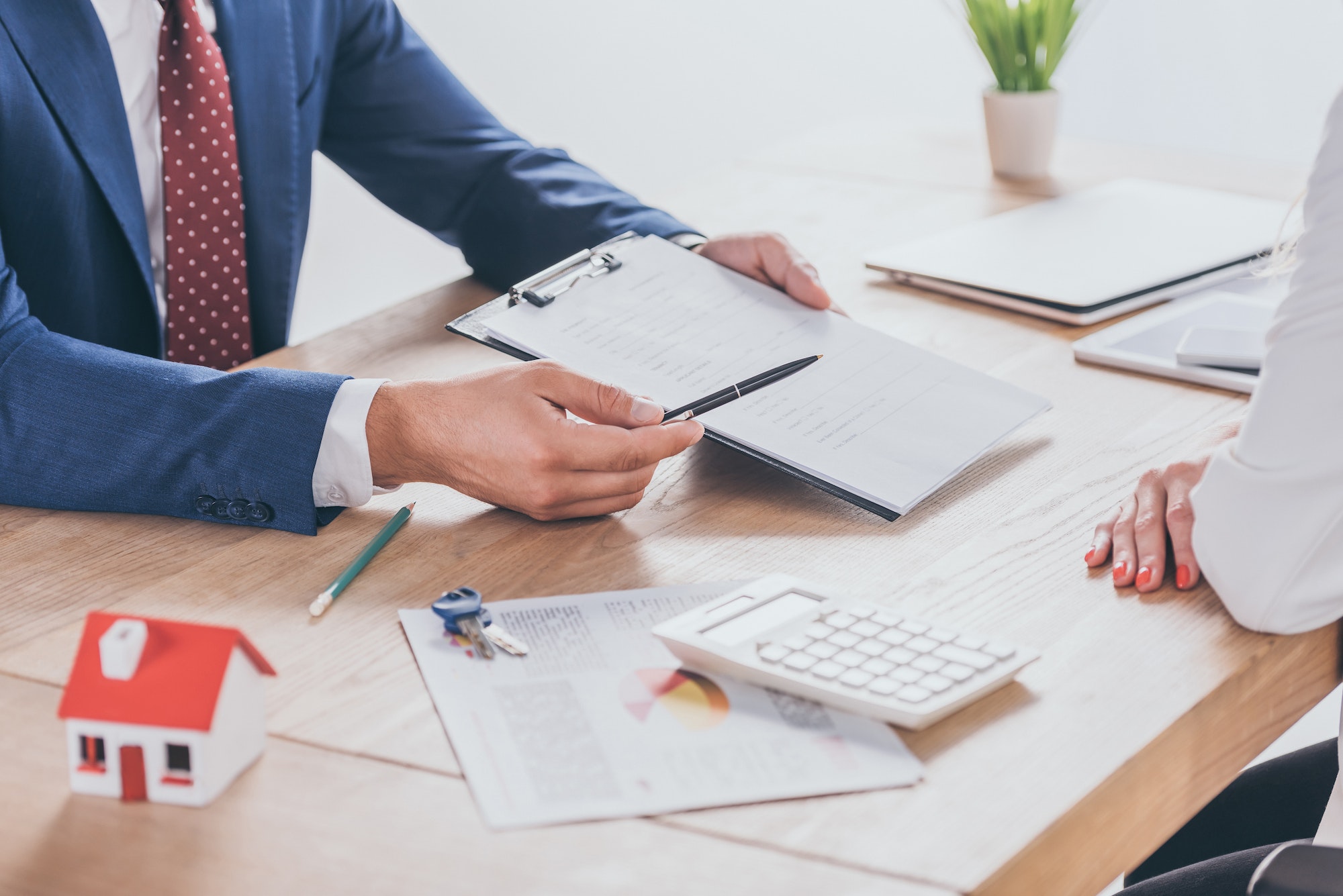 cropped view of man giving clipboard and pen to businesswoman while sitting at desk